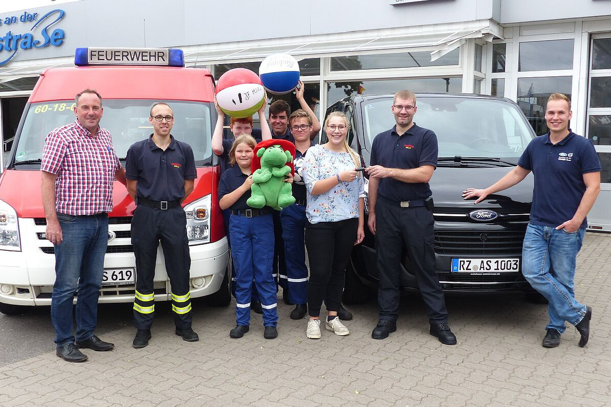 Neun Personen stehen vor einem PKW und einem Feuerwehrauto