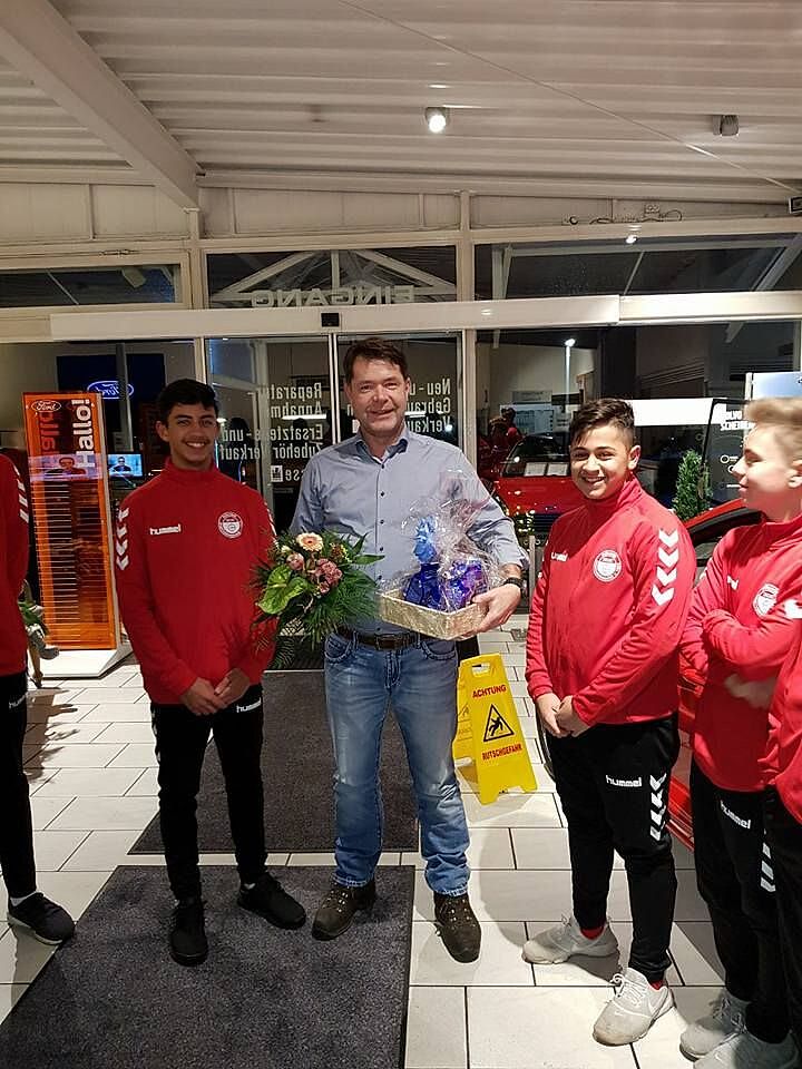 Mitglieder vom Fußballverein stehen neben einem Mann, der einen Blumenstrauß hält